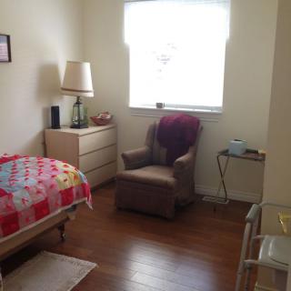 A cozy bedroom with a bed, chair, dresser, and window letting in natural light.