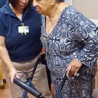 A healthcare worker assists an elderly woman using a walker.