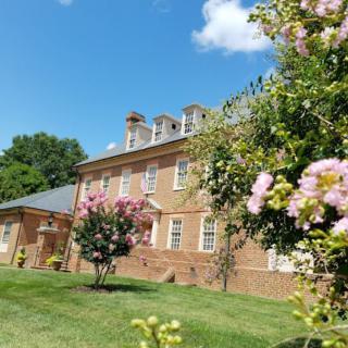 A historic brick building surrounded by blooming flowers and trees under a bright blue sky.