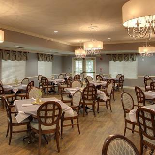 An elegant dining room with neatly arranged tables and chairs, featuring chandeliers for ambient lighting.