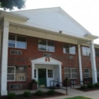 A two-story brick building with white columns and a gable roof.