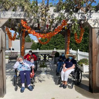 Elderly residents enjoying a sunny day outside, surrounded by autumn decorations.