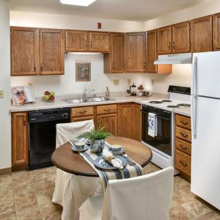 A cozy kitchen featuring wooden cabinets, complete with appliances and a small round dining table set for two.