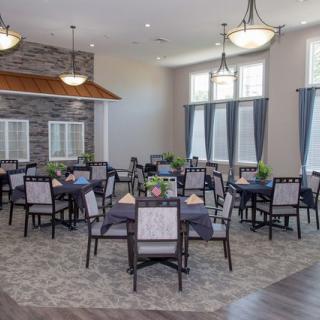 A spacious dining room with neatly arranged tables and chairs, featuring elegant lighting and large windows.