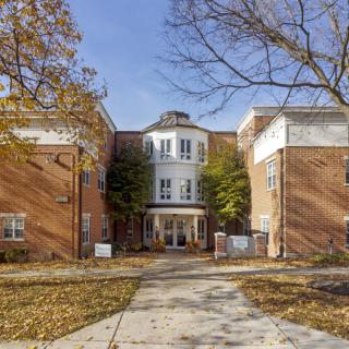 A brick building with an entrance surrounded by autumn trees and a pathway leading up to it.