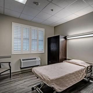 A clean and minimalist hospital room with a single bed and simple furnishings.