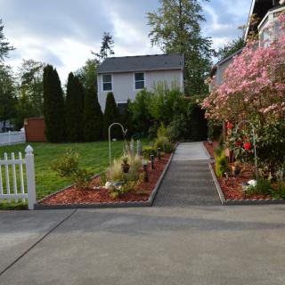 A beautifully landscaped garden with a pathway leading to a house, surrounded by flowers and greenery.