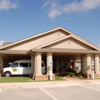 A building with a van parked under its covered entrance, featuring prominent columns and a surrounding parking area.