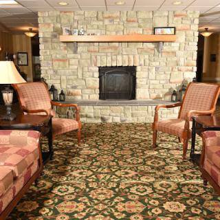 A cozy living room featuring a stone fireplace, armchairs, and a patterned rug.