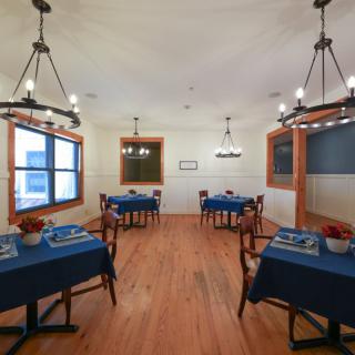 A cozy dining area with blue tablecloths, wooden floors, and elegant chandeliers.