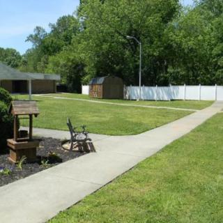 A well-maintained garden area with a concrete pathway, bench, and decorative well.