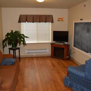 A cozy living room featuring a couch, chair, television, and a large window with a plant on a stand.