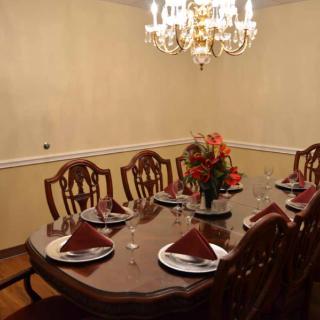 An elegantly set dining room table with a chandelier overhead and floral centerpiece.