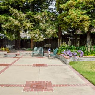 A spacious backyard patio area with outdoor seating, surrounded by trees and a flower garden.