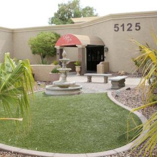 A building entrance with a garden featuring a fountain and palm trees.