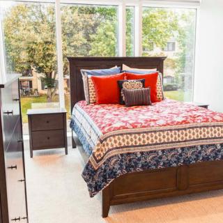 A brightly lit bedroom with a colorful bedspread and large windows.