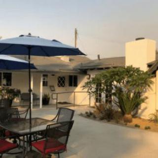 A sunny patio area with a table, chairs, and umbrellas outside a house.