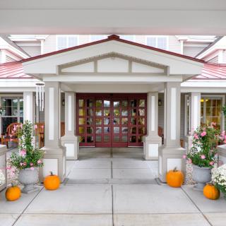 A welcoming building entrance decorated with pumpkins and flowers.