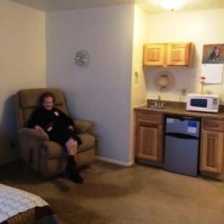 Woman sitting in a recliner in a small apartment with a kitchenette.