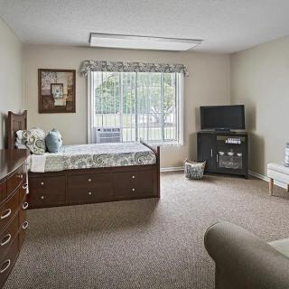 A cozy bedroom with a bed, dresser, and TV near a large window.