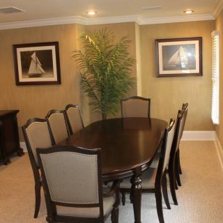 A dining room with an oval table, upholstered chairs, artwork on the walls, and a decorative plant.