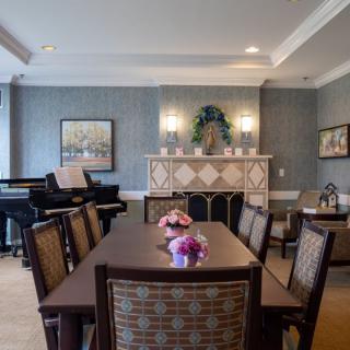 A well-decorated dining room with a wooden table and chairs, featuring a piano and elegant wall decor.