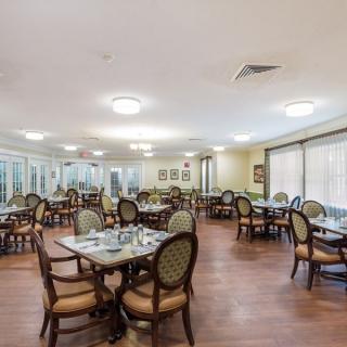 A spacious dining room with neatly arranged tables and chairs, featuring large windows and bright lighting.