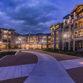 A beautifully lit residential building at night with a curved pathway leading to the entrance under a cloudy sky.