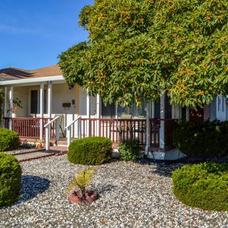 A charming house with a front porch and well-maintained landscaping, featuring a tree and rock garden.
