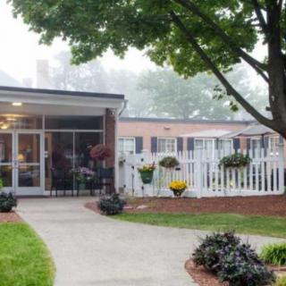 A quaint outdoor setting with a building surrounded by a garden, featuring a pathway and various plants.