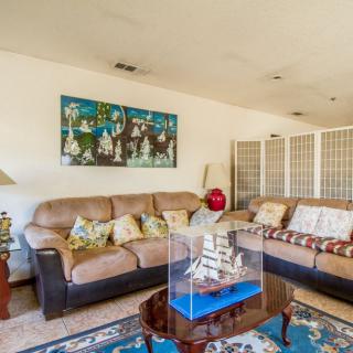 A cozy living room with a large couch and vibrant artwork, featuring a decorative ship model on the coffee table.