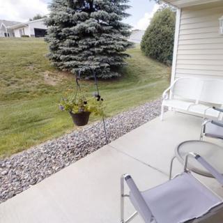 A cozy patio setup with chairs and a potted plant overlooking a grassy backyard with trees.