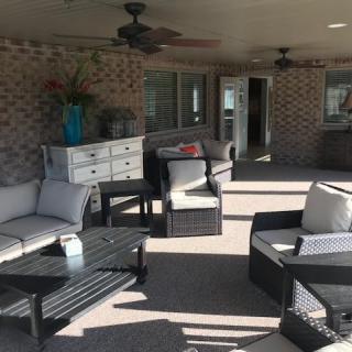 A comfortable outdoor patio with rattan furniture and ceiling fans, featuring a seating area against a brick wall.