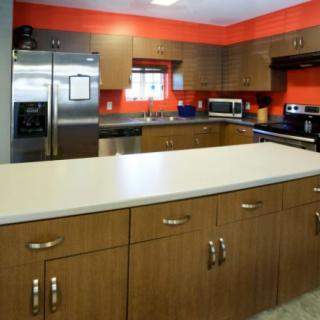 A modern kitchen with wooden cabinets and stainless steel appliances, featuring bright orange walls and a spacious countertop.