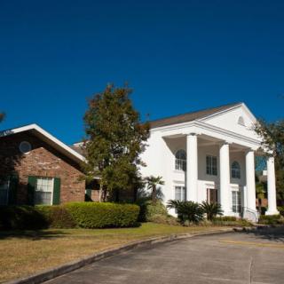 A suburban residential house with prominent white columns and a well-maintained lawn under a clear blue sky.
