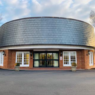 A modern circular building with large windows and a sleek roof, set against a cloudy sky.