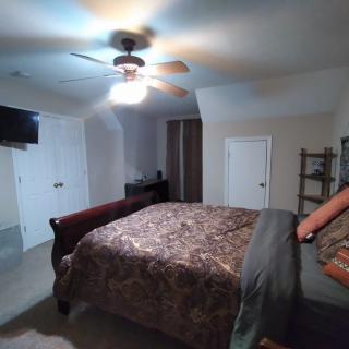 A cozy bedroom with a patterned bedspread, ceiling fan, and wall-mounted television.
