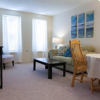 A cozy living room with a sofa, armchair, coffee table, and paintings on the wall.