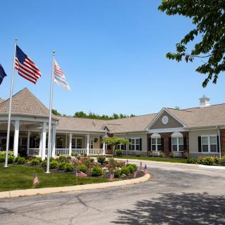 A single-story building with neatly maintained landscaping and multiple flags flying out front on a sunny day.