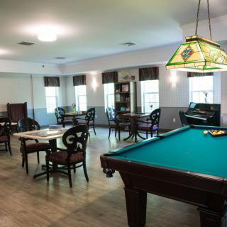 A spacious game room featuring a pool table, multiple tables and chairs, and stylish lighting.