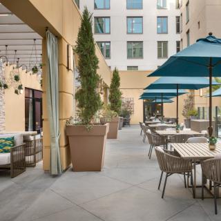 An inviting outdoor patio with tables and umbrellas, surrounded by plants in a courtyard setting.