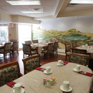 A restaurant dining area with tables set for service and a scenic mural on the wall.