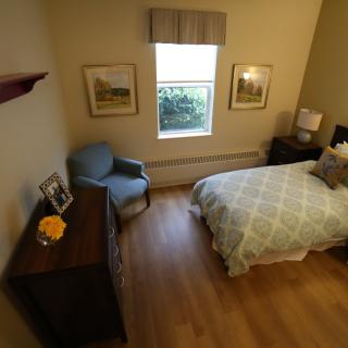 A cozy bedroom featuring a bed, chair, dresser, and window with wall decorations.