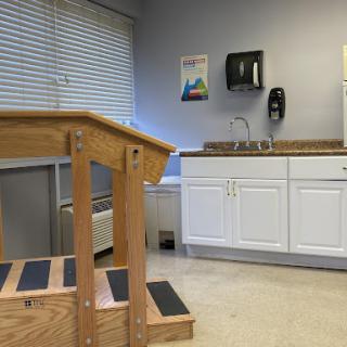 A view of a rehabilitation room featuring wooden stairs and a kitchenette area.