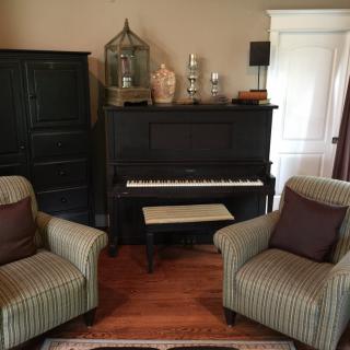 A cozy living room showcasing a black piano set against the wall, flanked by two striped armchairs on a wooden floor.