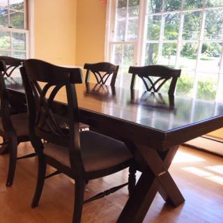 A sunlit dining room featuring a wooden table and matching chairs near large windows.