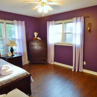 A cozy bedroom featuring elegant purple walls, ample natural light, and stylish furnishings.