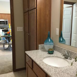 A bathroom with a granite countertop, featuring a sink, mirror, and decorative vase.