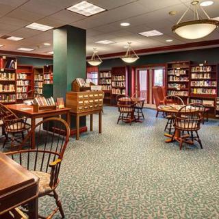 A cozy library with bookshelves, tables, and chairs arranged for reading.