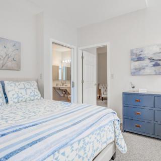 A modern bedroom featuring a bed with blue and white bedding, a dresser, and wall art in neutral tones.
